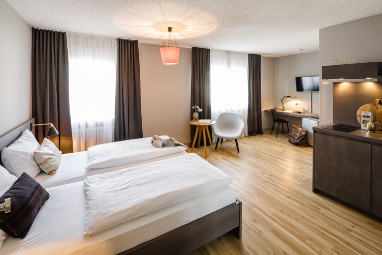 Ein Studio im Bold Hotel Frankfurt Messe mit Doppelbett und Küche Ein lichtdurchflutetes Hotelzimmer mit Holzboden und Doppelbett, großen Fenstern, Schreibtisch, Flachbildfernseher und Küchenzeile.
