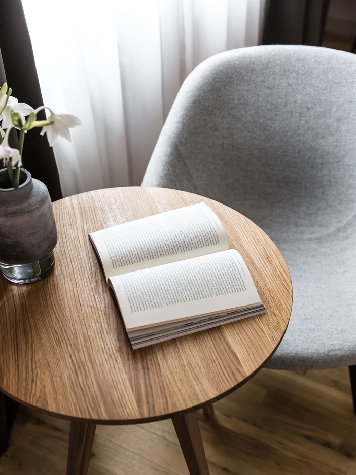 Light grey armchair with a small wooden table and an opened book on the table